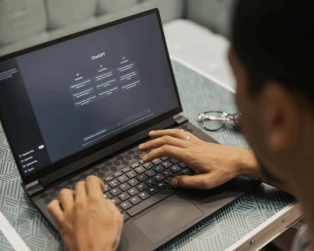 An over-the-shoulder photo of a man using a laptop displaying the homepage interface of ChatGPT