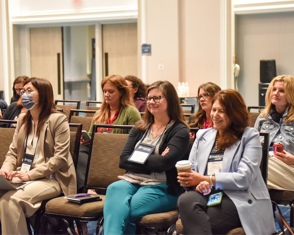 A group of women professionals sit together during a session at OLC Accelerate 2025. They are engaged with the presentation and exhibit a range of happy emotions.